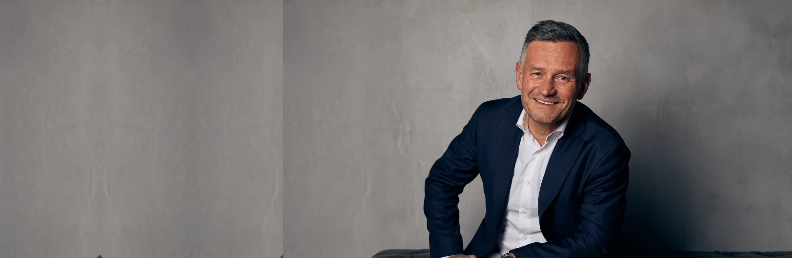 Coach in a light grey suit seated in a studio portrait, illustrating the INTP Logician MBTI profile
